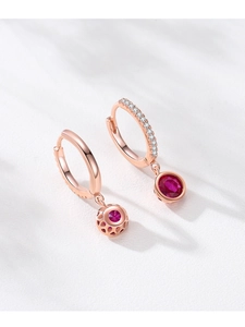 Macro detail of rose gold hoop earrings with red ruby charms and honeycomb metalwork