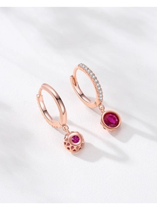 Détail macro de boucles d'oreilles rose doré avec gemme rouge et motif ajouré ciselé