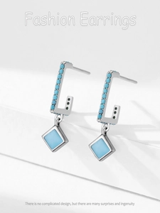 Macro detail of S925 silver C-shape earrings with turquoise stones and blue rhombus charms