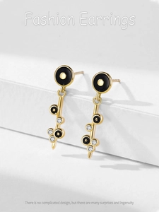 Detail of gold dangle earrings featuring black enamel discs and micro-set cubic zirconia