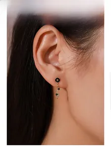 Detail of elegant gold drop earrings with black enamel and zircons on model's ear