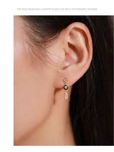Detailed view of dangling gold earrings with black enamel and diamonds on model