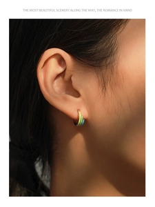 Detailed close-up of a silver U-shaped earring with rainbow enamel stripes on an ear lobe