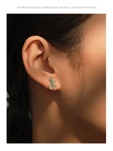 Macro shot of silver gecko earring with green enamel and sparkling zircon on earlobe