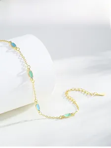 Detail of gold chain bracelet with blue and green enamel accents on a white stand