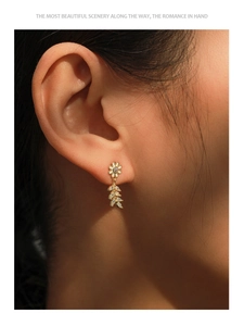 Detail of S925 silver daisy stud earring with zircon leaves worn on a female ear