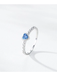 Detailed view of the twisted silver band and heart-shaped blue crystal on the ring
