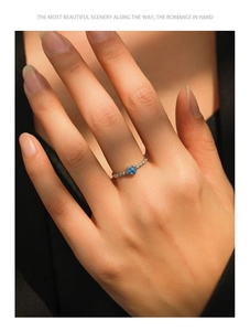 Detail of a blue heart-shaped gemstone ring with a twisted silver band on a model's finger