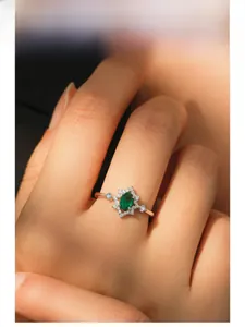 Detail of an oval emerald ring on a finger, featuring a vintage halo setting design