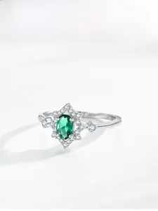 Macro detail of oval green emerald silver ring with shimmering halo and starburst setting