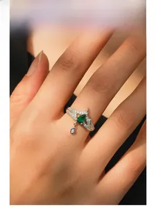 Macro of silver crown ring with pear-cut emerald stone and dangling drop on finger