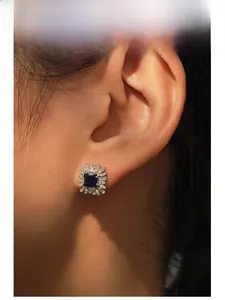 Detail view of square blue sapphire earrings with brilliant diamond halo on model ear