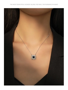 Détail d'un collier pendentif saphir carré avec halo de zircons porté sur un blazer noir