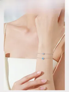 Detail of S925 silver bracelets with blue zircon flower and oval charms on model wrist