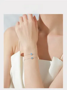 Detail of S925 silver bracelets with square and round blue zircon on a model's wrist