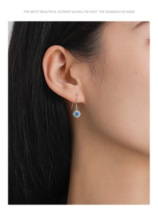 Macro shot of silver flower earrings featuring blue zircon center on a female model