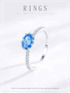 Detail of oval blue gemstone ring with zircon accents on a textured white background