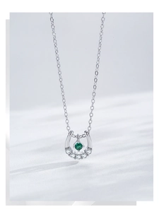 Macro detail of U-shape silver necklace featuring emerald gemstone and white zirconias