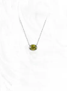 Macro detail of oval green gemstone pendant on a fine silver-tone chain necklace
