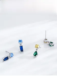Macro view of geometric silver earrings with blue sapphire and emerald teardrop stones