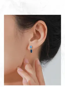 Close-up of model wearing silver earrings with round sky blue and rectangular deep blue sapphire