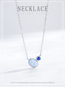 Macro shot of silver oval opal and blue gemstone pendant on a fine link chain necklace