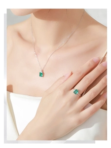 Close-up of emerald-cut green gemstone necklace and ring set on an elegant model