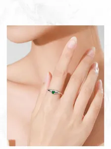 Close-up of a silver S925 heart-shaped green zircon ring worn by a model on stone background