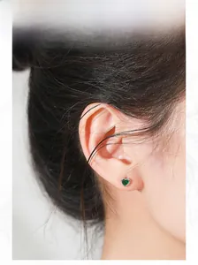 Detail view of a model wearing an elegant silver heart-shaped emerald stud earring
