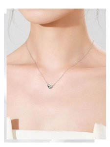 Gros plan d'un collier cœur en argent S925 avec zircon vert porté par une femme