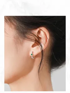 Gros plan d'une boucle d'oreille en argent S925 avec émeraude verte portée à l'oreille