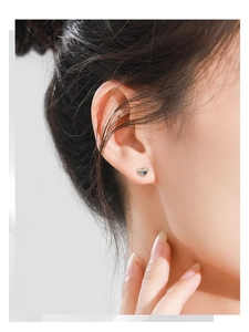 Close-up of heart-shaped silver earrings with small green zircon stone on earlobe