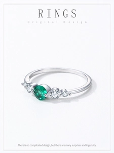 Macro shot of silver ring with green emerald stone and clear zircon side accents