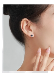 Close-up of heart-shaped blue sapphire stud earrings with silver plating on model