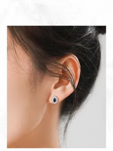 Close-up of elegant 925 silver stud earring with oval sapphire and halo crystals on ear