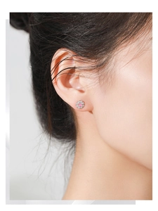 Detailed close-up of a flower-shaped 925 silver earring with pink gem on woman's earlobe