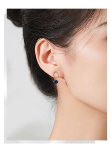 Detail of silver earring on model featuring an oval stud and round blue cubic zirconia
