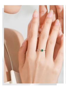 Détail d'une bague ouverte en argent 925 avec zircon vert émeraude sur le doigt d'un mannequin
