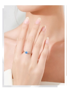 Detailed view of a silver ring with a round blue gemstone on a finger