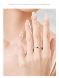 Detail of a slim silver ring featuring a round deep blue sapphire on a woman's hand