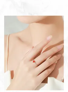 Nahaufnahme eines zarten S925-Silberrings mit kleinem roten Emaille-Herz am Finger der Frau