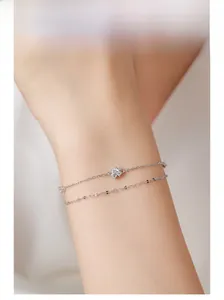 Detailed view of dual-layer silver bracelet with small blue floral zircon charm on model