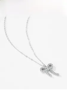 Détail du collier noeud en argent avec pierres scintillantes sur fond gris texturé