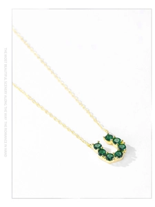 Dettaglio macro del ciondolo a U dorato con zirconi verde smeraldo su catena in argento