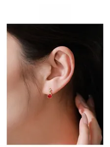 Close-up of model wearing gold stud earrings with round red zircon and claw setting
