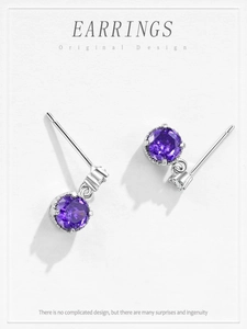 Macro view of purple zircon stud earrings in silver prong setting on grey texture