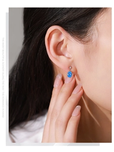Détail d'une boucle d'oreille en pierre bleue ovale et petit diamant sur modèle