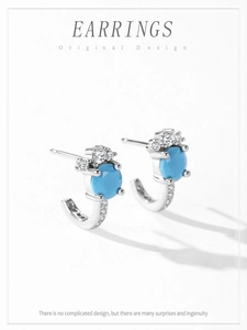 Macro shot of silver J-shaped earrings with turquoise stone and white zircon details