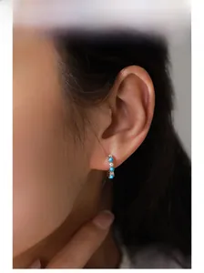 Détail de créoles en argent avec pierres turquoise et zircons blancs sur l'oreille