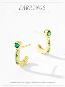 Detail of gold C-shaped earrings with green and white cubic zirconia on white background